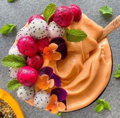 a smoothie topped with fruit and flowers on top of a gray table next to a spoon