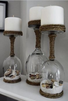 three glass vases with sand and shells in them sitting on a shelf next to candles