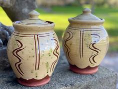 two ceramic jars sitting on top of a rock