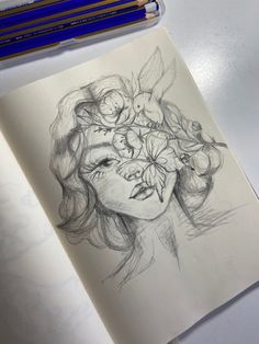 a drawing of a woman's face with flowers in her hair and two pencils next to it