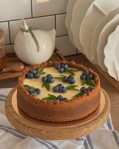 a cheesecake with blueberries and green leaves on top sits on a wooden platter