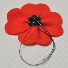 a red flower with black beads on it sitting on a piece of paper next to thread