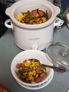 a crock pot filled with corn and green beans next to a bowl of soup