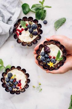 two hands holding small desserts with berries and blueberries in them on a marble surface