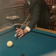 a man in a suit leaning over a pool table to hit a ball with a cue