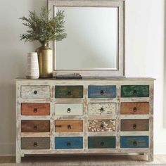 an old dresser with multicolored drawers and a mirror on the top, next to a potted plant