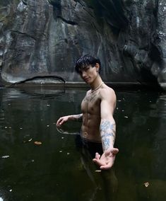 a shirtless man standing in the water with his hand out to touch something off