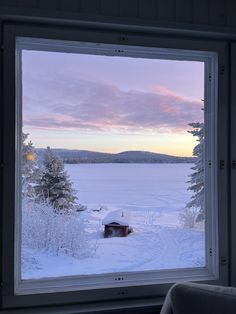 a window view looking out onto a snowy field with trees in the foreground and a cabin on the far side