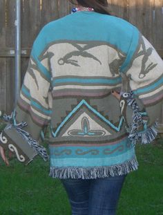 a woman walking in the grass wearing a sweater with dolphins on it and fringes around her shoulders