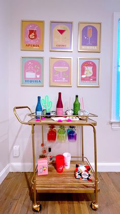 a gold bar cart with drinks on it in front of some framed pictures and posters