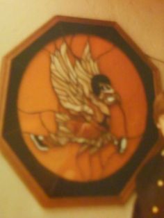 an orange and black clock with a bird on it's face next to a wall