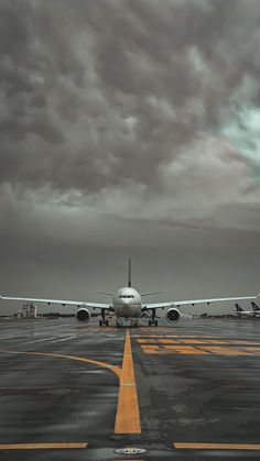 an airplane sitting on the tarmac under a cloudy sky with yellow lines in front of it