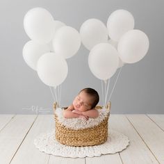 a baby sleeping in a basket with white balloons