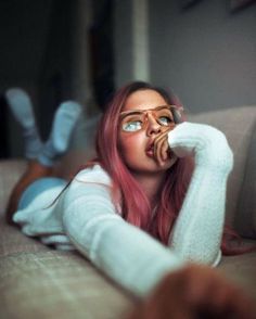 a woman with pink hair and glasses laying on a couch looking up at the camera