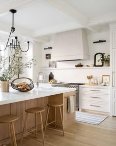 a white kitchen with wooden stools and an island in front of the stove top