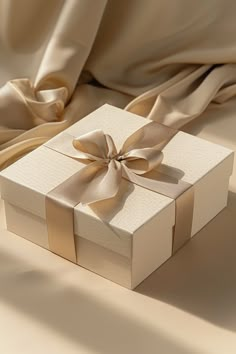 a white box with a gold bow on it sitting on a beige cloth covered bed