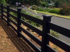 a black fence is next to the road and flowers are growing on the side of it