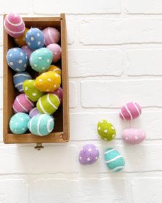 a wooden box filled with colorfully painted easter eggs next to some smaller ones on a white brick wall