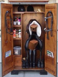 an open wooden horse shoe cabinet with boots and saddles