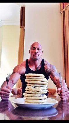 a man sitting in front of a stack of pancakes on top of a table with a knife and fork