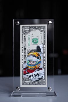 a dollar bill with the image of a race driver on it is in a clear acrylic frame