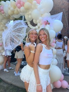 two young women standing next to each other under an arch with balloons and umbrellas