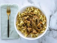 a white bowl filled with pasta and meat on top of a table next to a fork