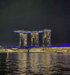 some very tall buildings in the middle of water at night with bright lights on them