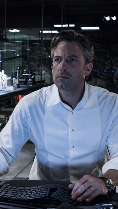 a man sitting at a desk in front of a keyboard and monitor with his hand on the keyboard