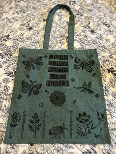 a green tote bag sitting on top of a bed covered in flowers and butterflies