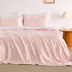 a bed with pink sheets and pillows in a room next to a lamp on a table