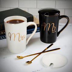 two coffee mugs sitting on top of a table next to books and a mouse