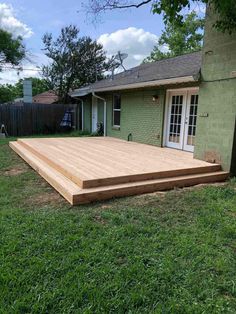 a wooden deck in front of a house with green walls and grass on the ground