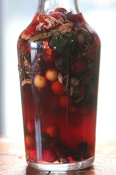 a bottle filled with liquid sitting on top of a wooden table next to leaves and berries