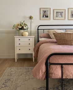 a bed with pink sheets and pillows in a bedroom next to a white chest of drawers