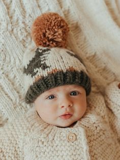 a baby wearing a knitted hat laying on top of a blanket