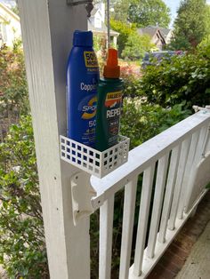 two sunscreens are hanging on the side of a white porch railing near bushes