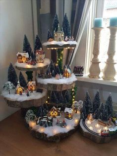 a christmas tree with lights and houses in the snow next to a window sill