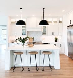 a large kitchen with white cabinets and black pendant lights over the island, along with three stools