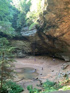 some people are standing in the water near a large rock formation with a waterfall coming out of it