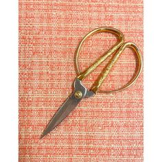 a pair of scissors sitting on top of an orange and white table cloth with gold handles