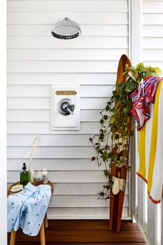 there is a surfboard leaning against the wall next to a towel rack and potted plant