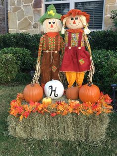 two scarecrows standing next to each other in front of a house with pumpkins and hay