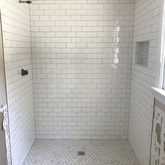 a white tiled shower stall with the door open