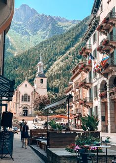 people are walking down the street in front of buildings with mountains in the back ground