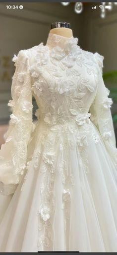 a white wedding dress with long sleeves and flowers on the skirt is displayed in front of a