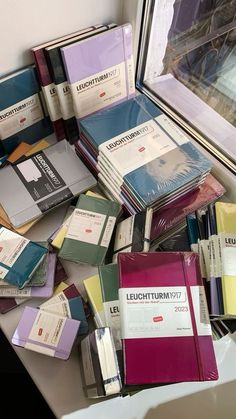 many books are stacked on top of each other in front of a window sill