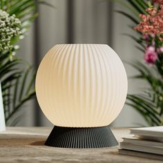 a white lamp sitting on top of a wooden table next to some flowers and books