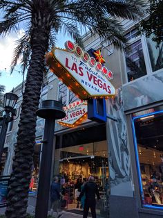 the las vegas sign is lit up at night in front of a building with palm trees