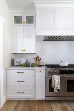 a kitchen with white cabinets and stainless steel stove top oven, wood flooring and wooden floors